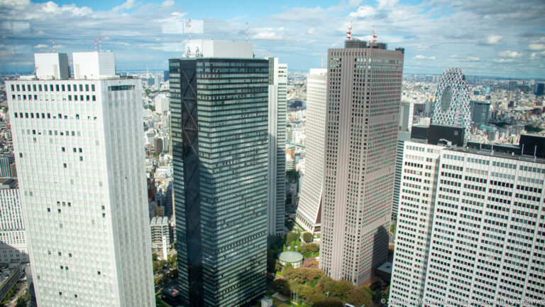 Elevated view of four closely spaced Shinjuku towers with contrasting pale, dark, and brown façades.