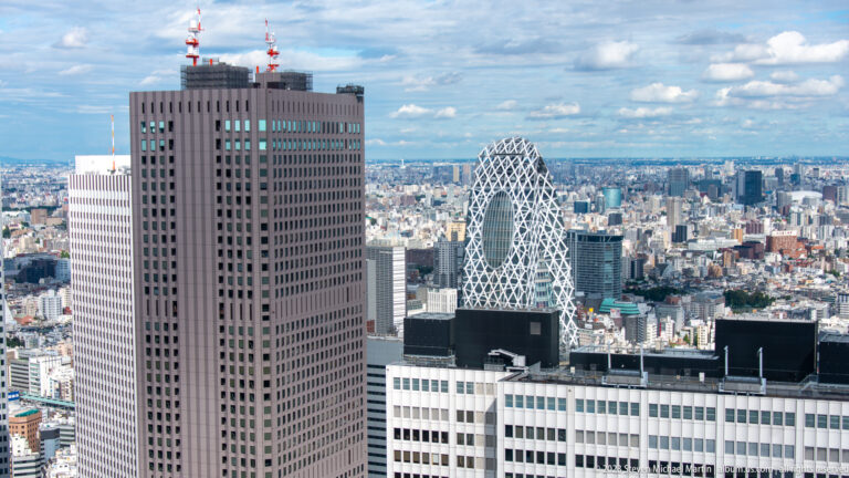 Brown rectangular tower with rooftop antennas, with the white-latticed Cocoon Tower visible behind it.