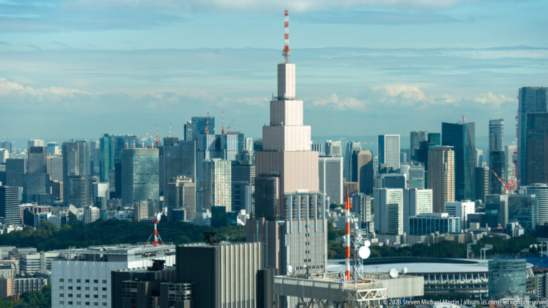 Telephoto skyline view centered on the stepped NTT Docomo Yoyogi Building and its antenna.