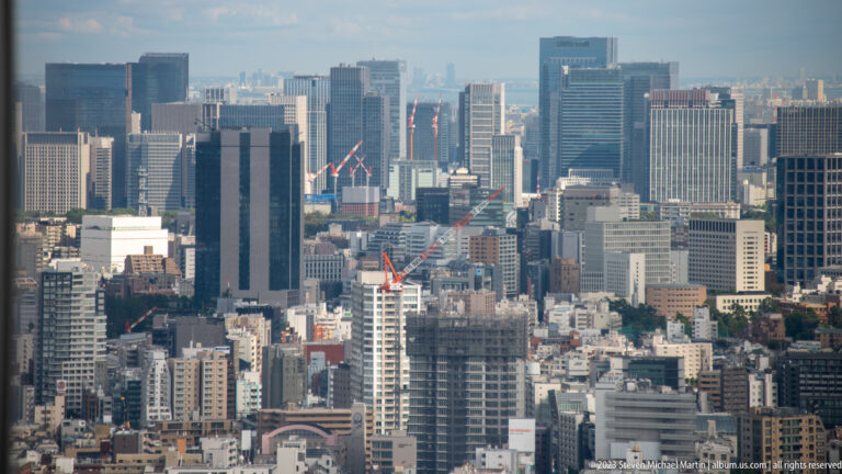 Telephoto city view of clustered office towers, cranes, and dense low-rise buildings in central Tokyo.