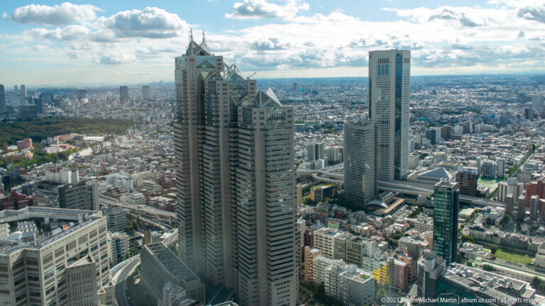 Oblique aerial view of Shinjuku Park Tower, a neighboring slender tower, and dense western Tokyo.