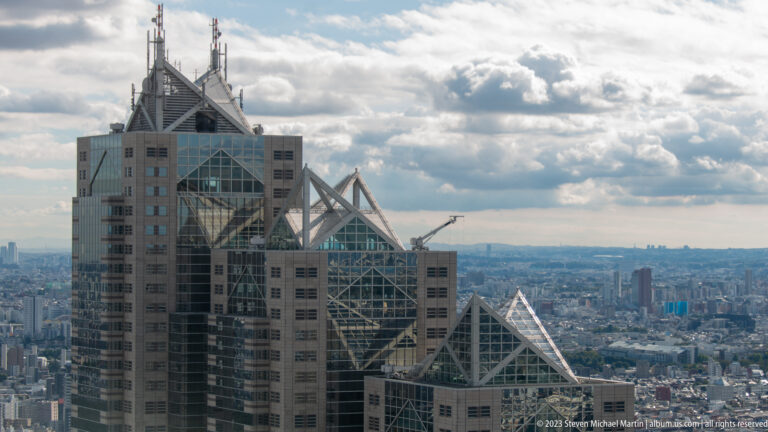 Close view of Shinjuku Park Tower’s stepped upper floors and triangular structural crowns.