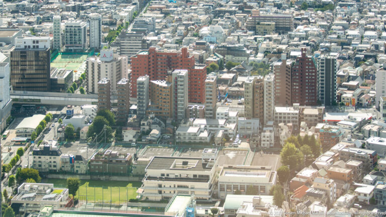 Apartment towers, low-rise homes, school buildings, and a green athletic field seen from above.