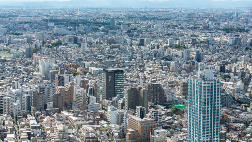 Blue residential tower above dense low- and mid-rise neighborhoods stretching across western Tokyo.