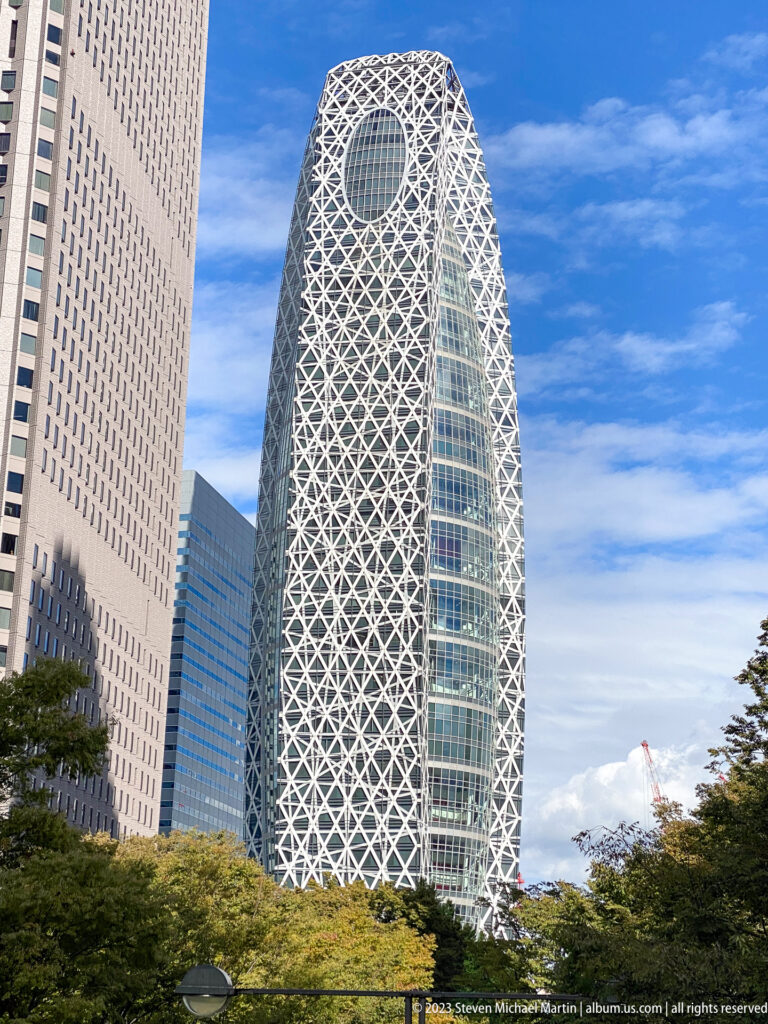 Mode Gakuen Cocoon Tower with white diagonal lattice and oval crown opening above trees.
