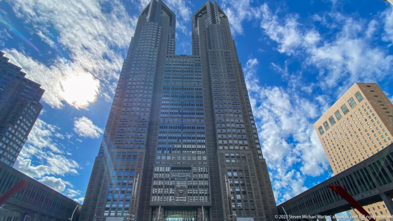 Low-angle view of the Tokyo Metropolitan Government Building twin towers against blue sky and clouds.