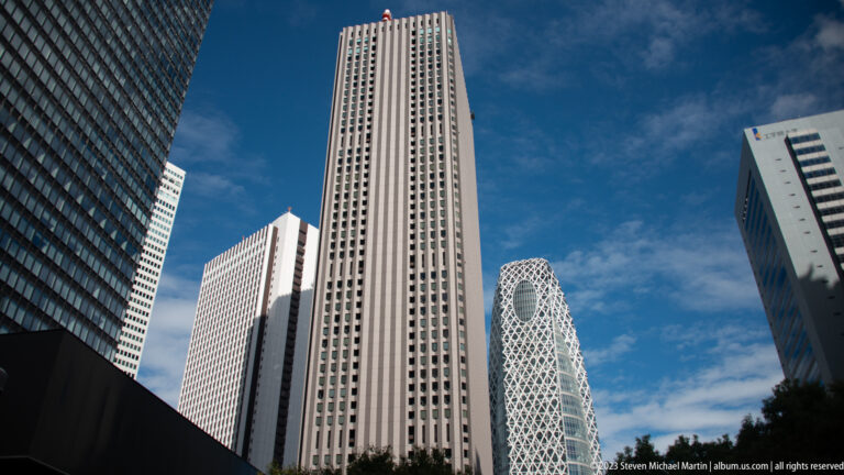 Upward view between Shinjuku towers, with the Mode Gakuen Cocoon Tower visible in the background.