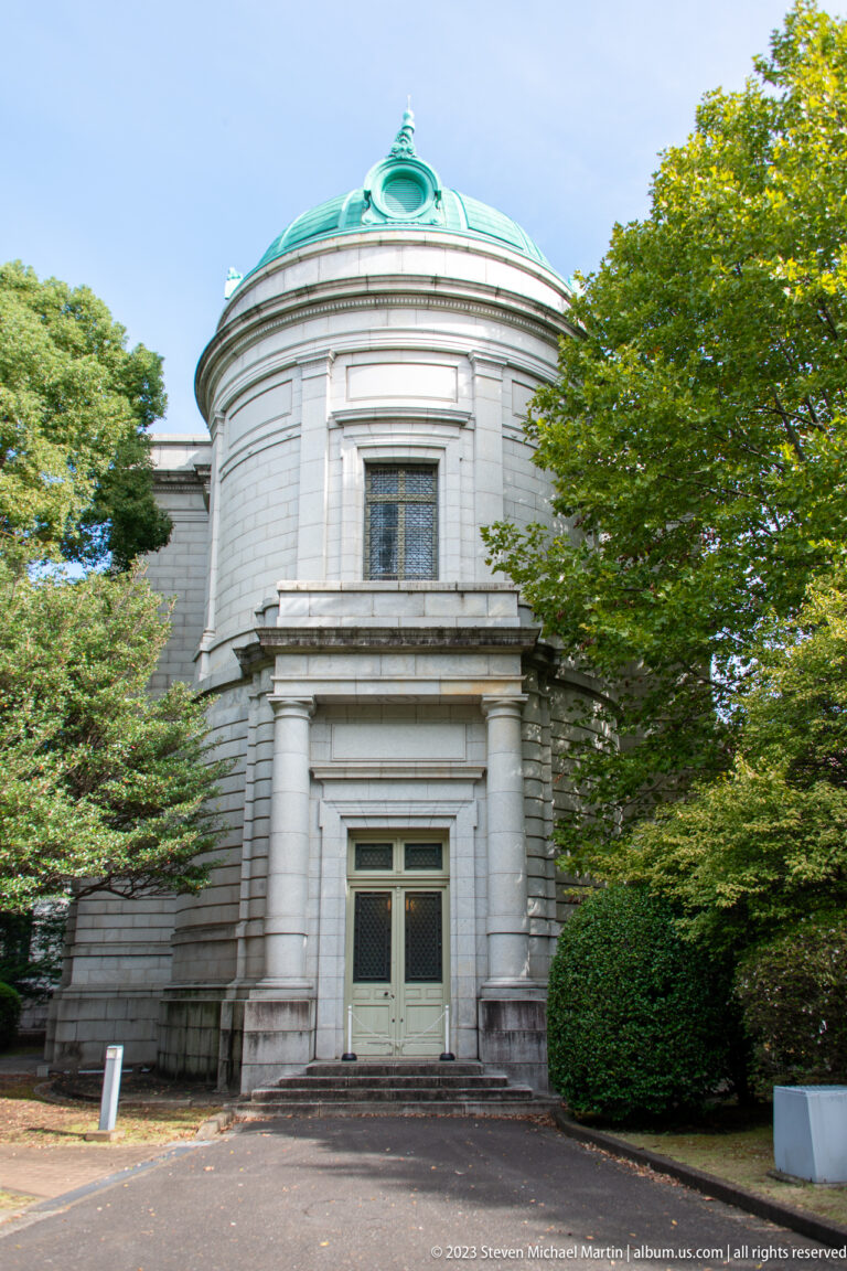 Rounded stone entrance pavilion of the Hyokeikan with columns, green copper dome, trees, and a central doorway.