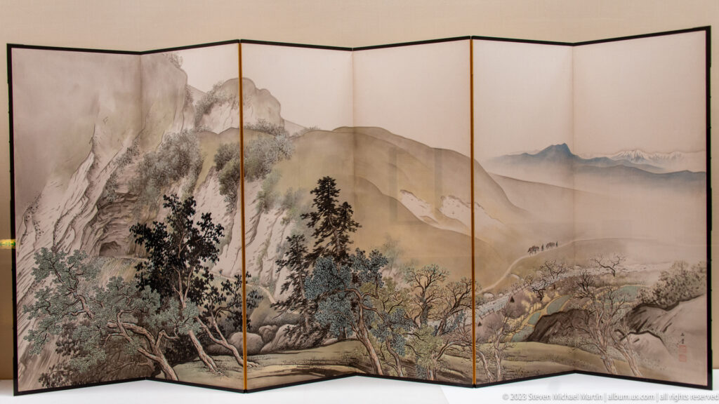 Multi-panel folding screen painted with trees, mountains, rocky slopes, and mist.