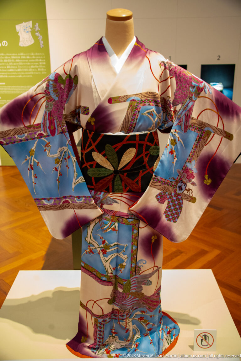 Colorful formal kimono with cranes, flowers, ribbons, geometric patterns, and a black obi.