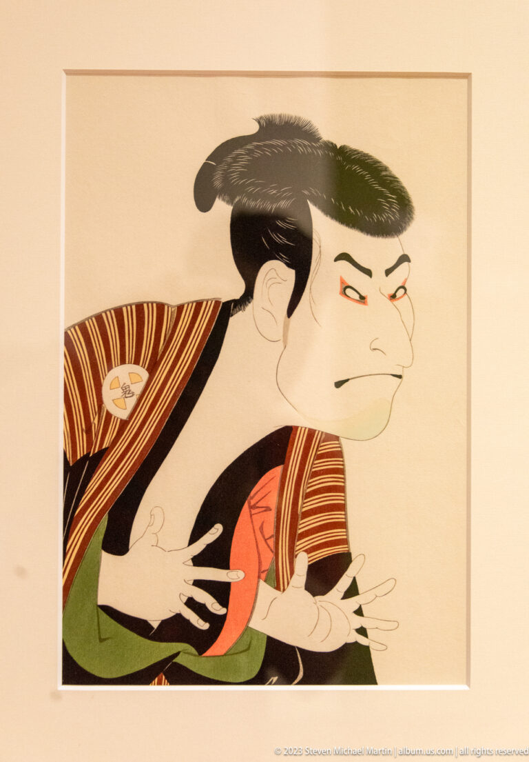 Ukiyo-e print of a kabuki actor in profile with dramatic hands and striped robes.