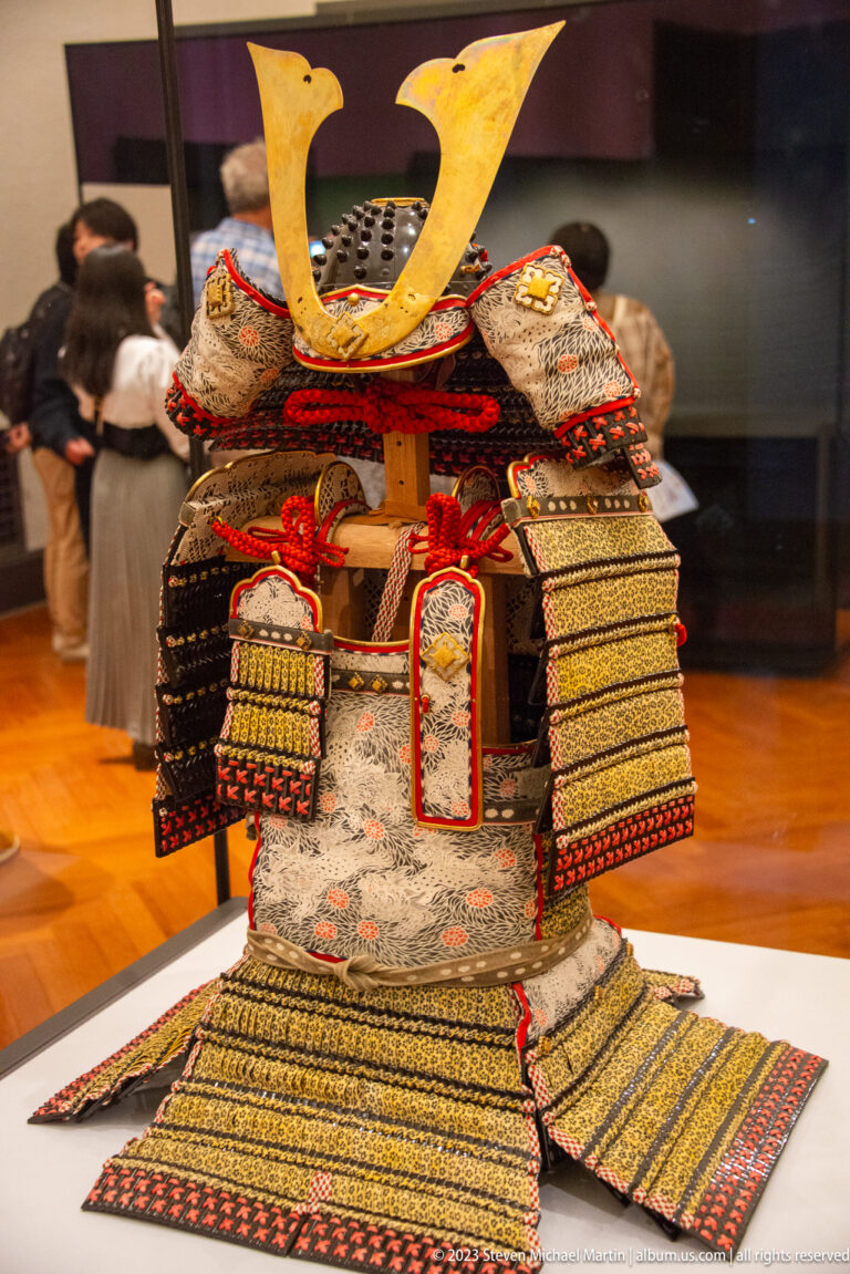 Complete samurai armor with large gold horned helmet crest, layered plates, and red lacing.