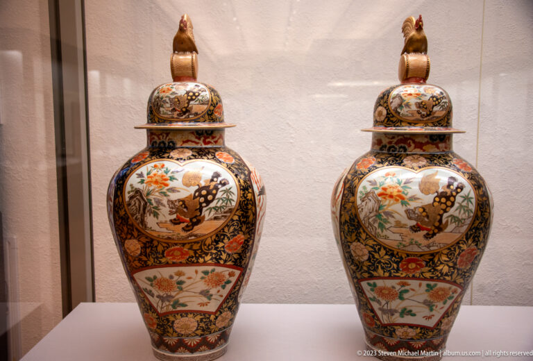 Pair of matching porcelain covered jars with bird finials and multicolored floral decoration.
