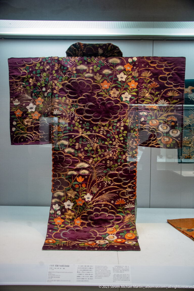 Purple kimono with dense multicolored embroidery of flowers, foliage, and looping bands.