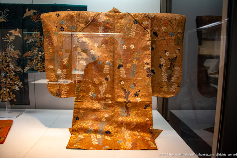 Orange-gold brocade robe with broad sleeves and scattered floral motifs in blue, white, and green.