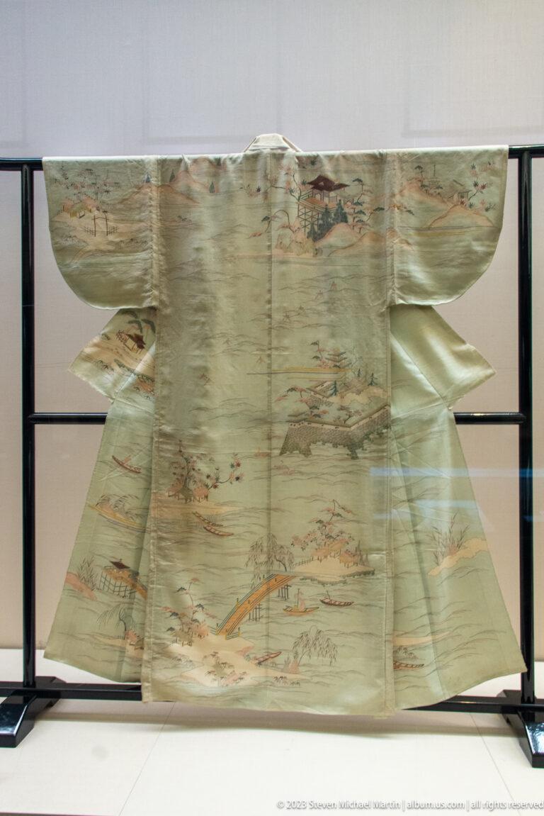 Pale kimono decorated with bridges, rivers, buildings, trees, and small figures.
