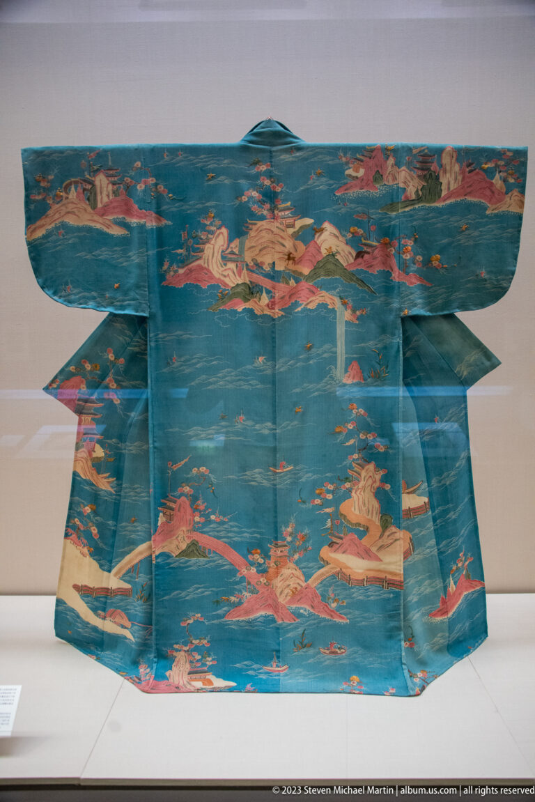 Turquoise kimono decorated with pink and gold mountains, water, trees, and small figures.