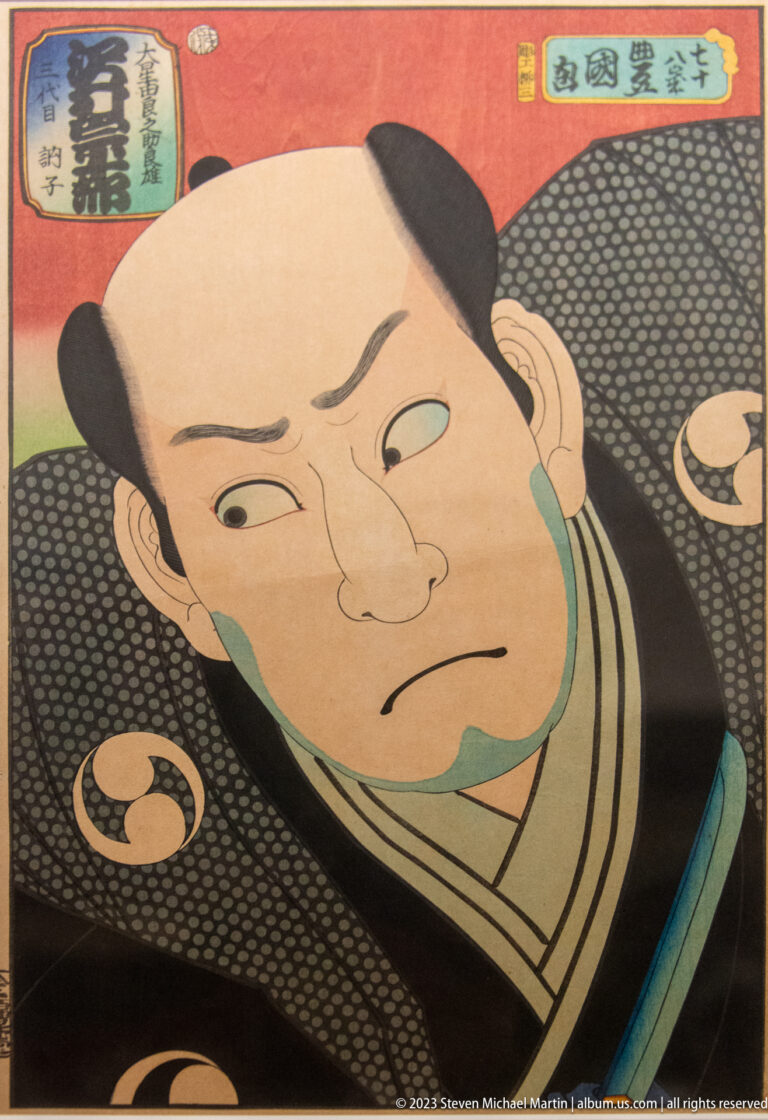 Ukiyo-e bust portrait of a stern kabuki actor with shaved forehead, green accents, and patterned black robe.