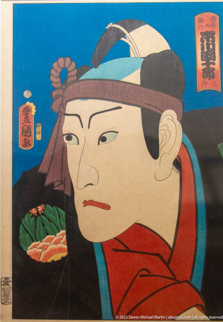 Color woodblock portrait of a kabuki actor in red robe and headband against a blue background.
