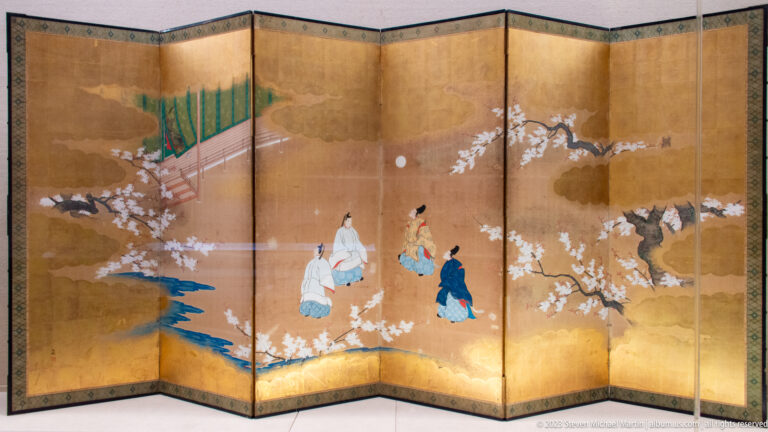 Gold folding screen with robed figures, flowering trees, water, and architectural details.