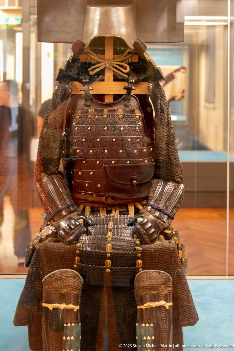 Dark samurai armor with domed helmet, lamellar plates, shoulder guards, and gold fittings.