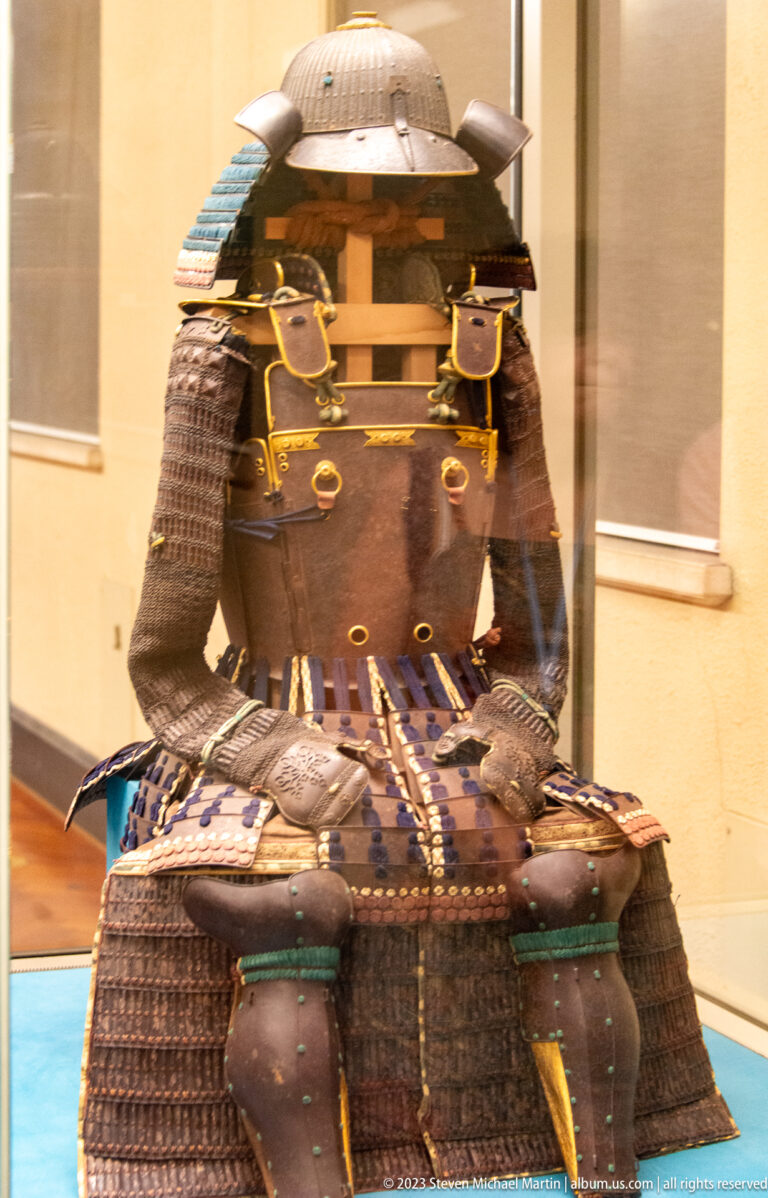 Dark samurai armor with rounded helmet, gold trim, and blue-laced skirt plates.