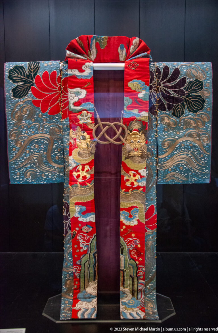 Open-front theatrical costume with red floral bands, blue wave-patterned sleeves, and purple interior.