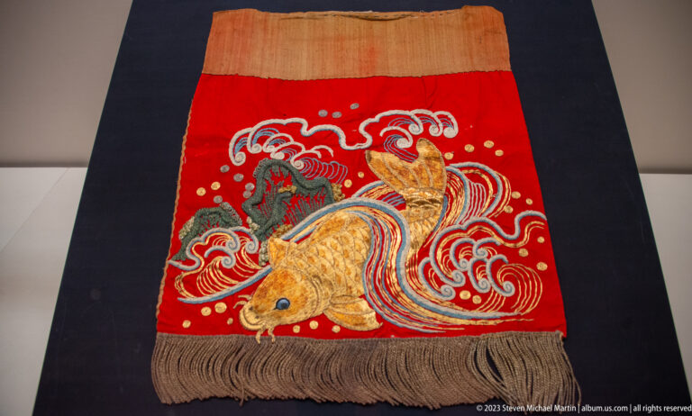 Red embroidered panel with tiger, dragon, curling waves, and long fringe.