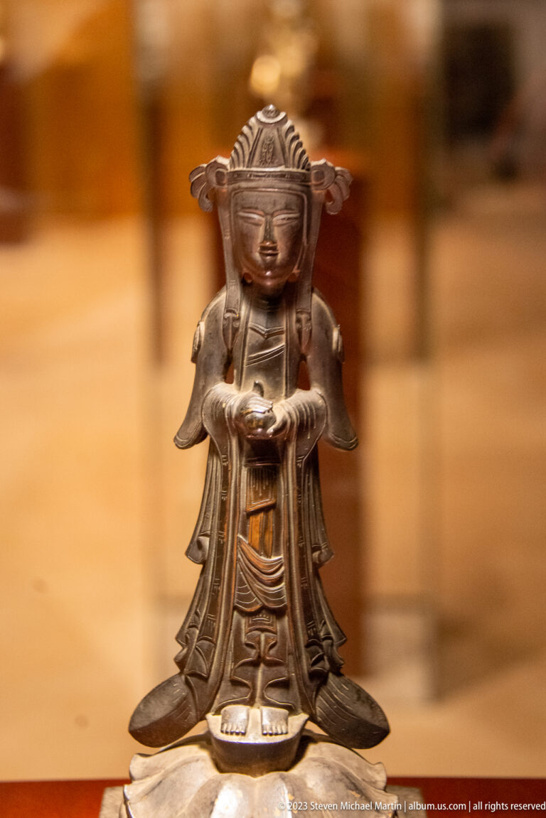 Small crowned gilt-bronze figure with cupped hands and broad wing-like forms at the shoulders.