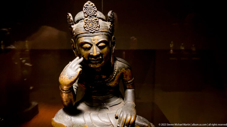 Seated crowned Buddhist figure touching the cheek with two fingers.