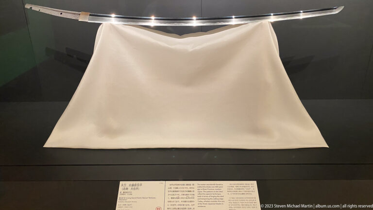 Curved polished Japanese sword blade displayed horizontally above a white support cloth.