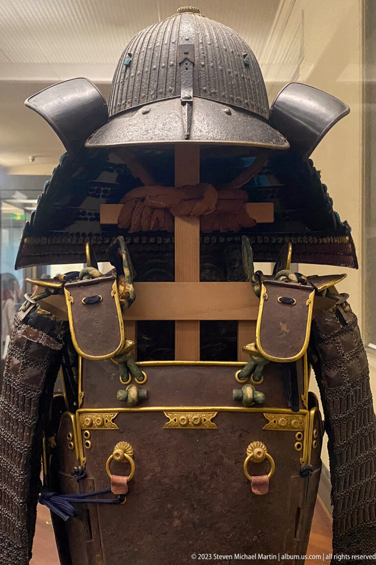 Rear view of samurai armor with domed helmet, shoulder guards, cuirass, and wooden support.