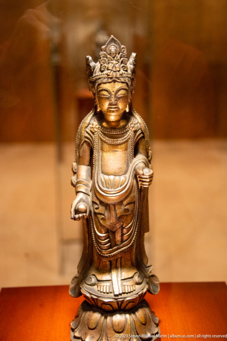 Small golden Buddhist figure on a lotus base with both hands open at waist height.