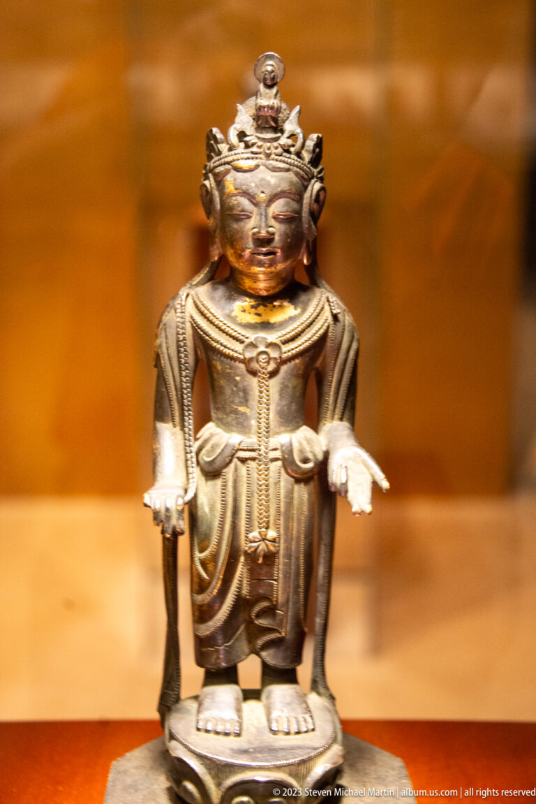 Small golden crowned Buddhist figure standing with both hands extended at different heights.