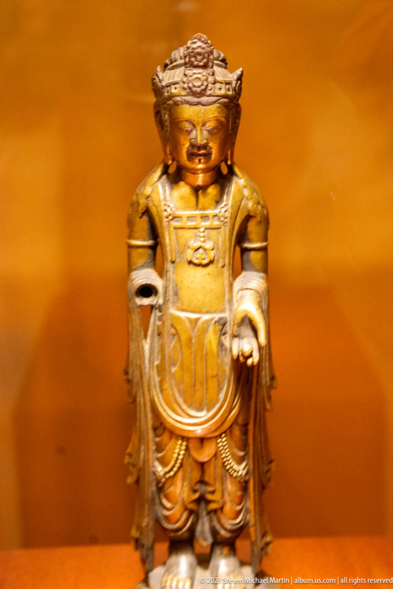 Golden crowned Buddhist figure standing with one hand lowered and the other palm open.