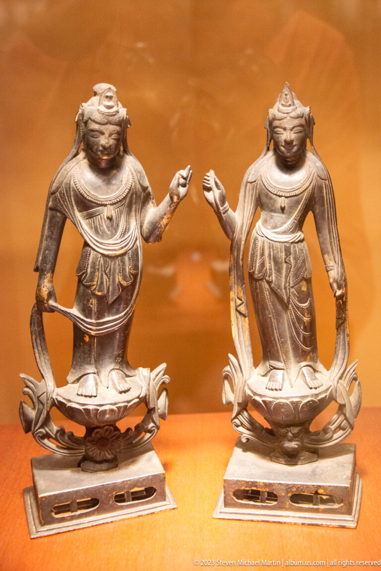 Pair of bronze kneeling Buddhist attendants on lotus bases with raised hands.