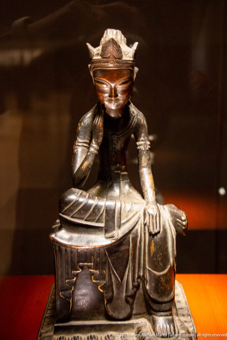 Seated bronze Buddhist figure leaning its head on one hand with the other hand on the knee.