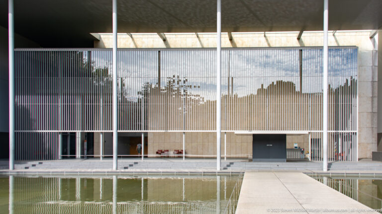 Centered frontal view of the Horyuji gallery’s vertical screen, recessed doorway, white frame, and reflecting pool.