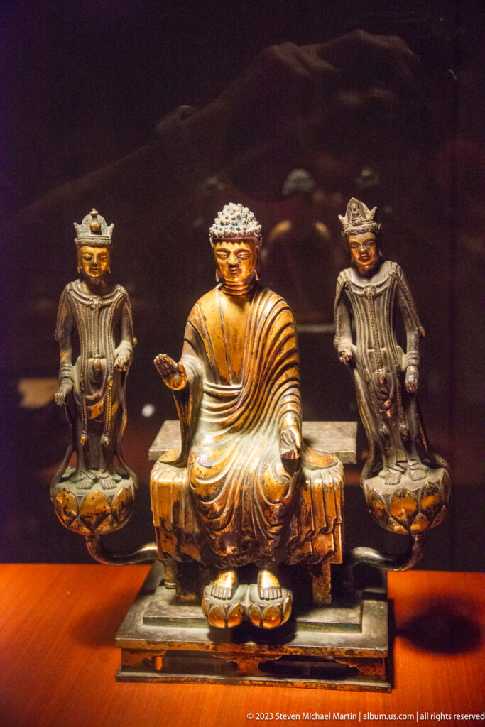 Seated Buddha centered between two smaller standing attendants on lotus bases.
