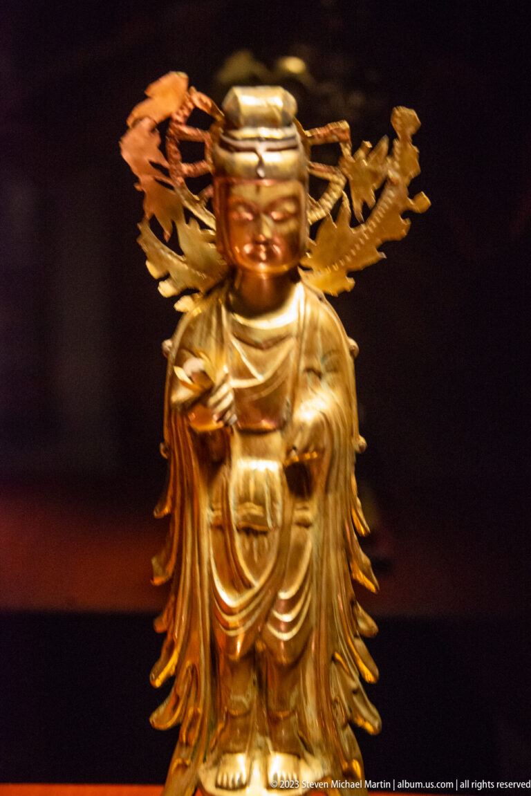 Golden standing Buddhist figure framed by elaborate openwork ornament extending outward like wings.