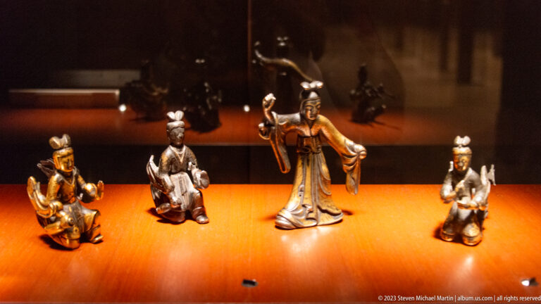 Four small bronze Buddhist figures, both seated and standing, arranged together in a museum case.