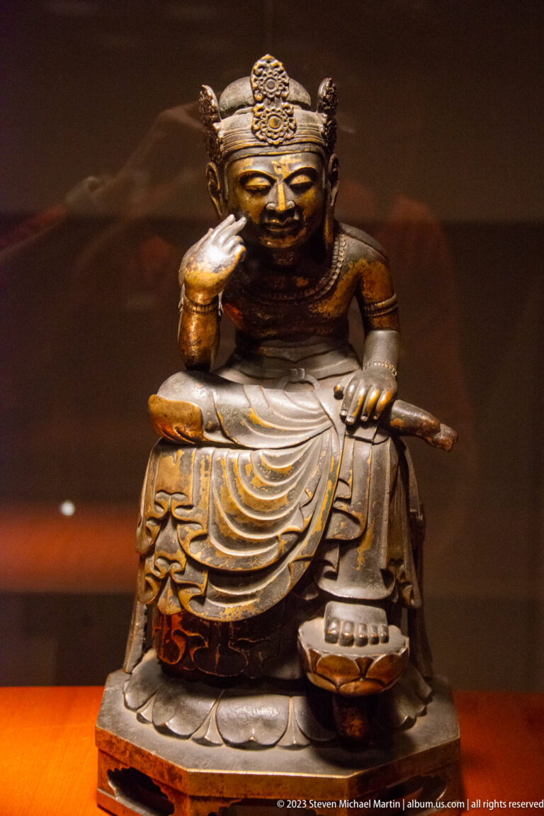 Seated crowned bronze Buddhist figure resting one hand against the cheek.