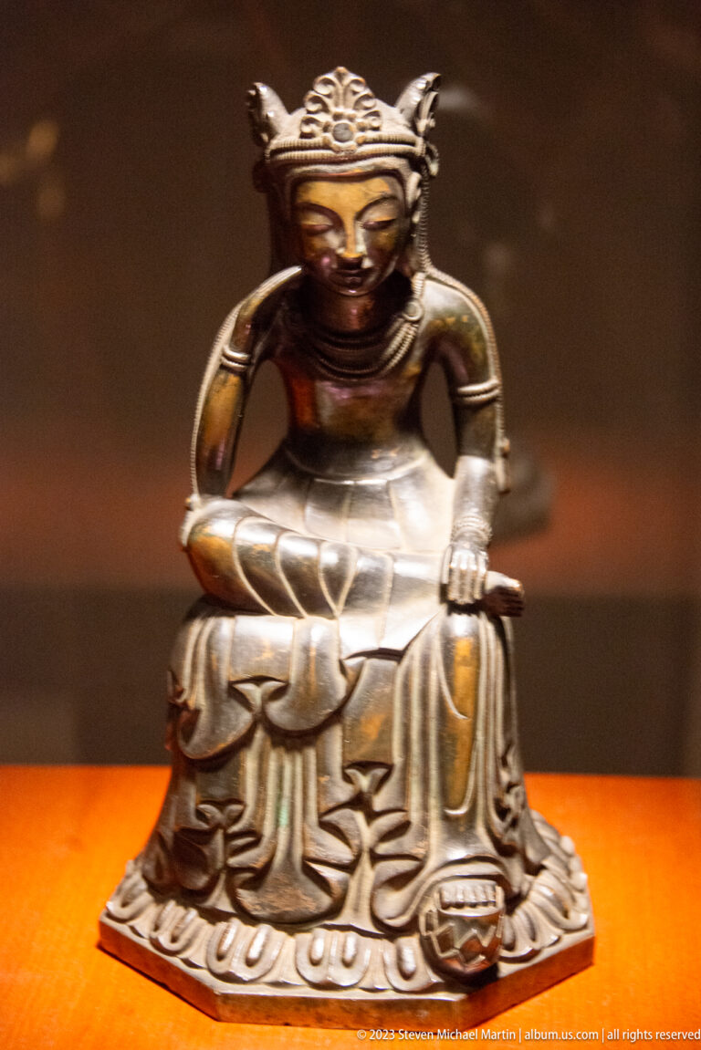 Seated bronze Buddhist figure supporting the head with one hand, with lotus-patterned drapery.
