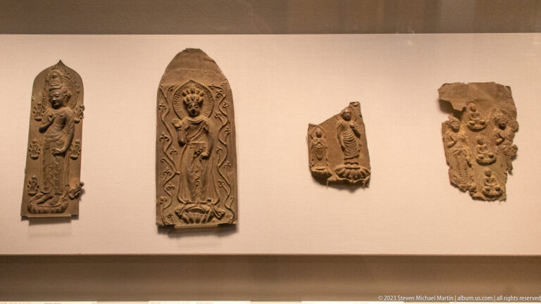 Four fragmentary Buddhist relief plaques with standing and seated figures mounted on a wall.