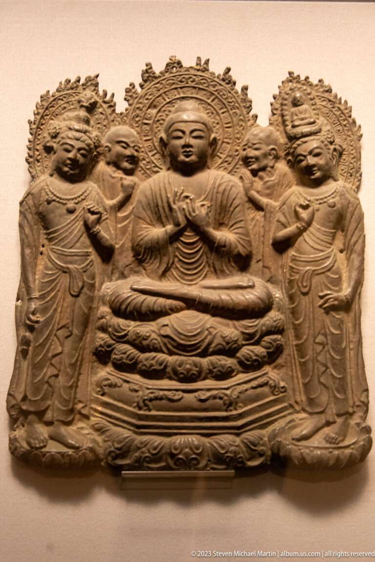 Rectangular Buddhist relief with a seated central Buddha and two haloed standing attendants.