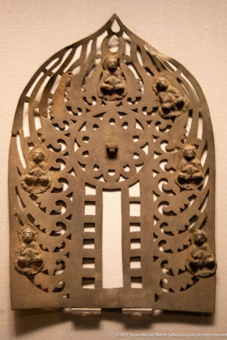 Arched openwork bronze panel with a central opening and small Buddhist figures around the border.