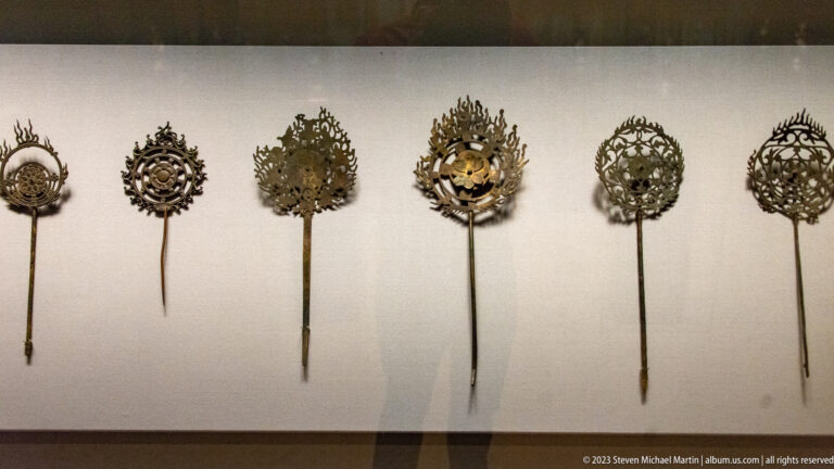 Six long-handled metal ritual ornaments with different openwork emblems displayed in a row.