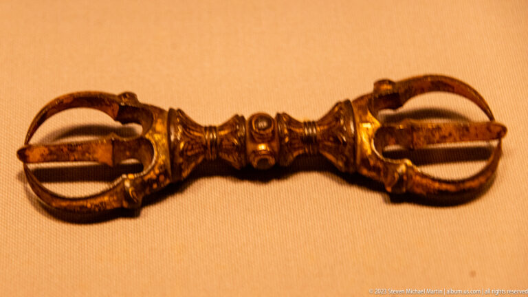 Double-ended metal vajra with curved prongs and a decorated central grip.