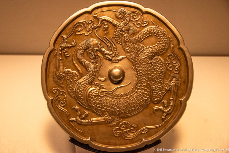 Circular high-tin bronze mirror back with central boss, radiating waves, islands, animals, and figures.