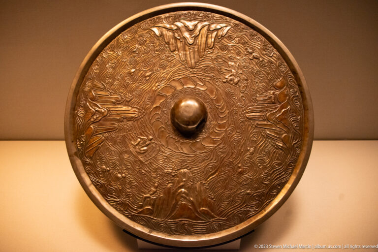 Round bronze mirror back with central knob and dense radiating wave-like decoration.